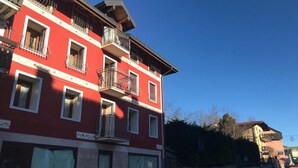 Un bâtiment rouge doté de nombreux balcons et fenêtres, un mur de pierre et un ciel d’un bleu limpide.