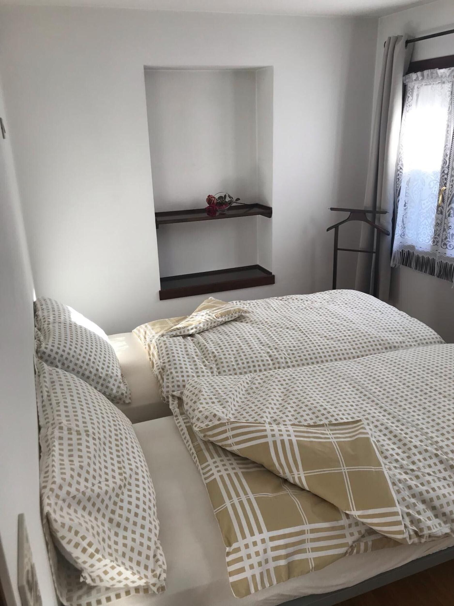A bedroom with a bed, two shelves, a hanging rack, and a window with curtains.