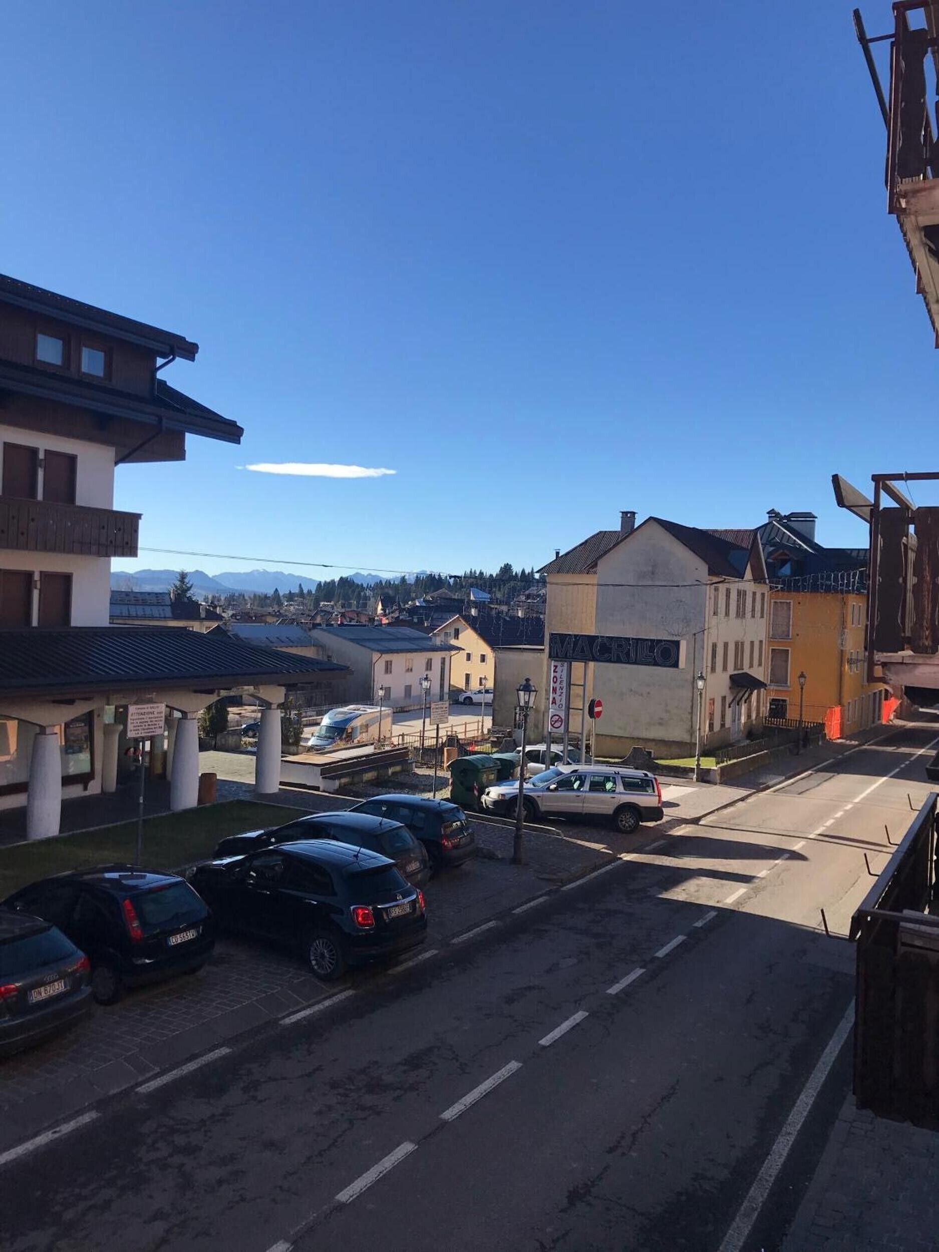 A street view with parked cars, buildings, and a clear sky.