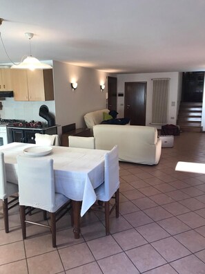 Ein Essbereich mit Tisch und Stühlen, eine Küche mit Herd und Schränken, ein Wohnzimmer mit Sofa sowie eine Treppe, die zu einer oberen Etage führt.