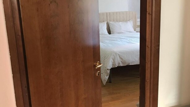 Une porte en bois donne sur une chambre à coucher qui contient un lit, une tête de lit et une table de chevet.