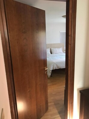 Une porte en bois donne sur une chambre à coucher qui contient un lit, une tête de lit et une table de chevet.