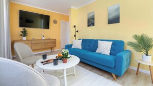A living room with a blue sofa, a white coffee table, a grey armchair, and a television mounted on the wall. - Colorful Apartment in Wisla | 2 Bedrooms | Workspace. (Wisła)