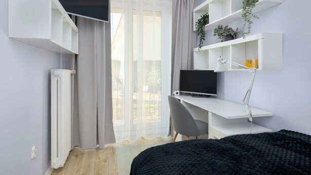 A modern bedroom with a bed, a desk with a computer, a chair, and built-in shelving with plants. - Colorful Apartment in Wisla | 2 Bedrooms | Workspace. (Wisła)