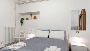 Ein ordentlich eingerichtetes Schlafzimmer mit Bett, Nachttischen, einem Sessel, einem Heizkörper und einem Regal mit Dekoration.