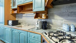 Una cocina con gabinetes color turquesa, estufa a gas, microondas, tostadora y cafetera.