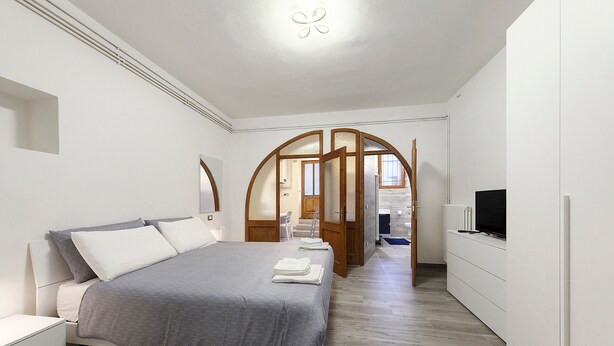 Un dormitorio con una cama, televisión y baño visibles a través de un arco.