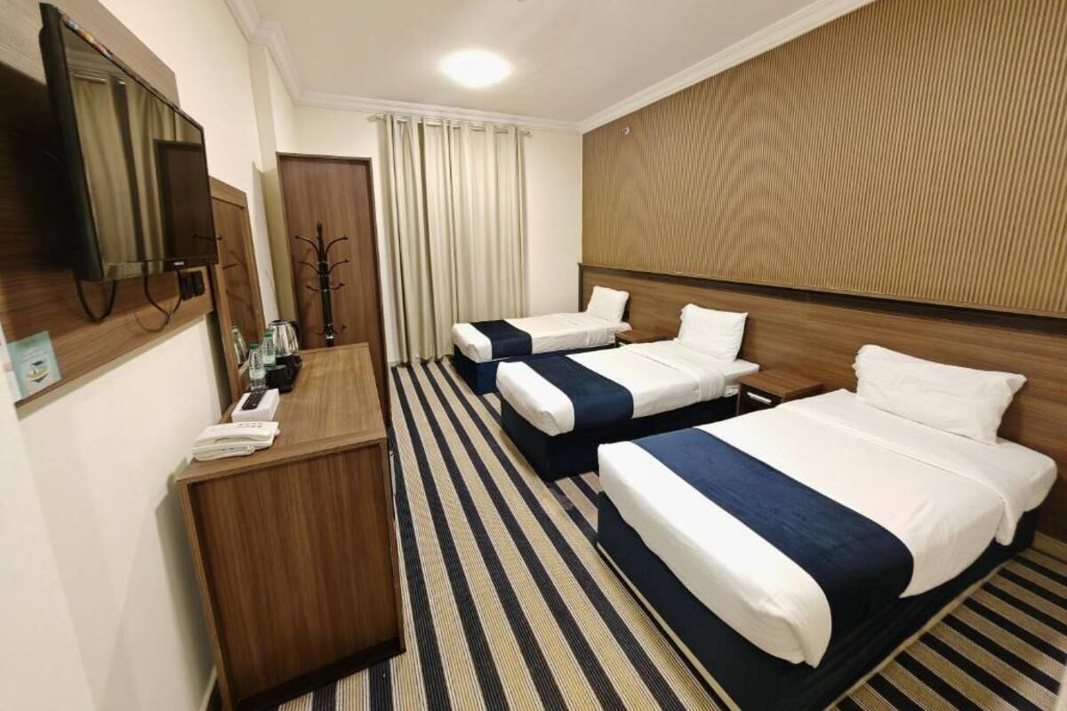 Habitación de hotel con dos camas, cabecero de madera, televisión de pantalla plana, escritorio y perchero.