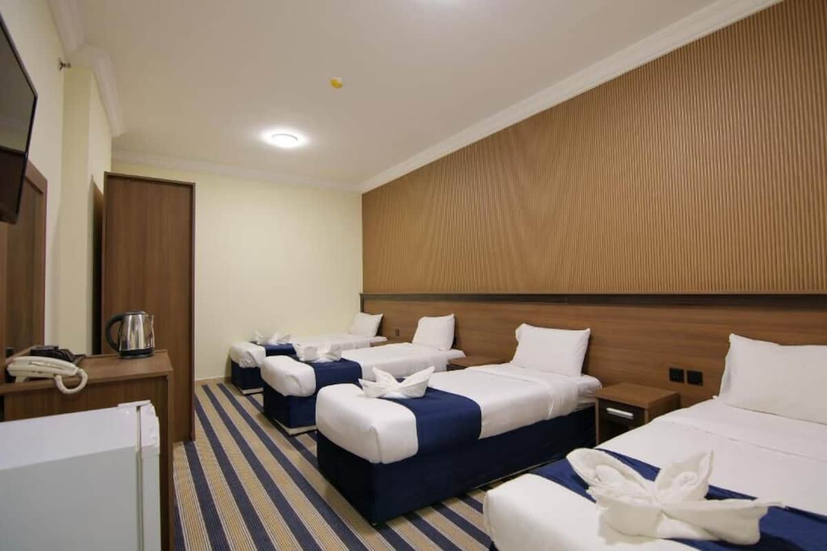 Habitación de hotel con tres camas, cabecera de madera, escritorio con teléfono y cafetera.