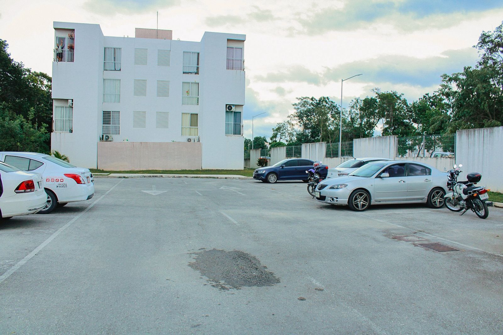 A parking lot with several cars and a motorcycle, a modern building with multiple windows, and a clear sky.