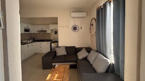 Una sala de estar moderna con un sofá seccional gris oscuro, una mesa de centro de madera y una cocina al fondo.