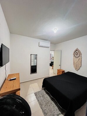 Une chambre à coucher comprenant un lit, un téléviseur, un miroir, un climatiseur et un élément décoratif mural.