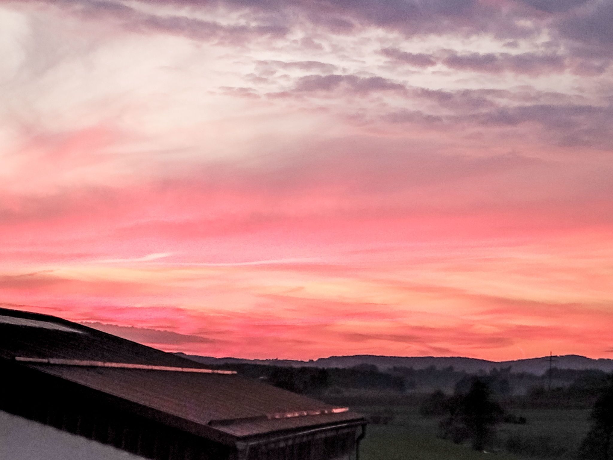 A sunset over a rural landscape with a building in the foreground.