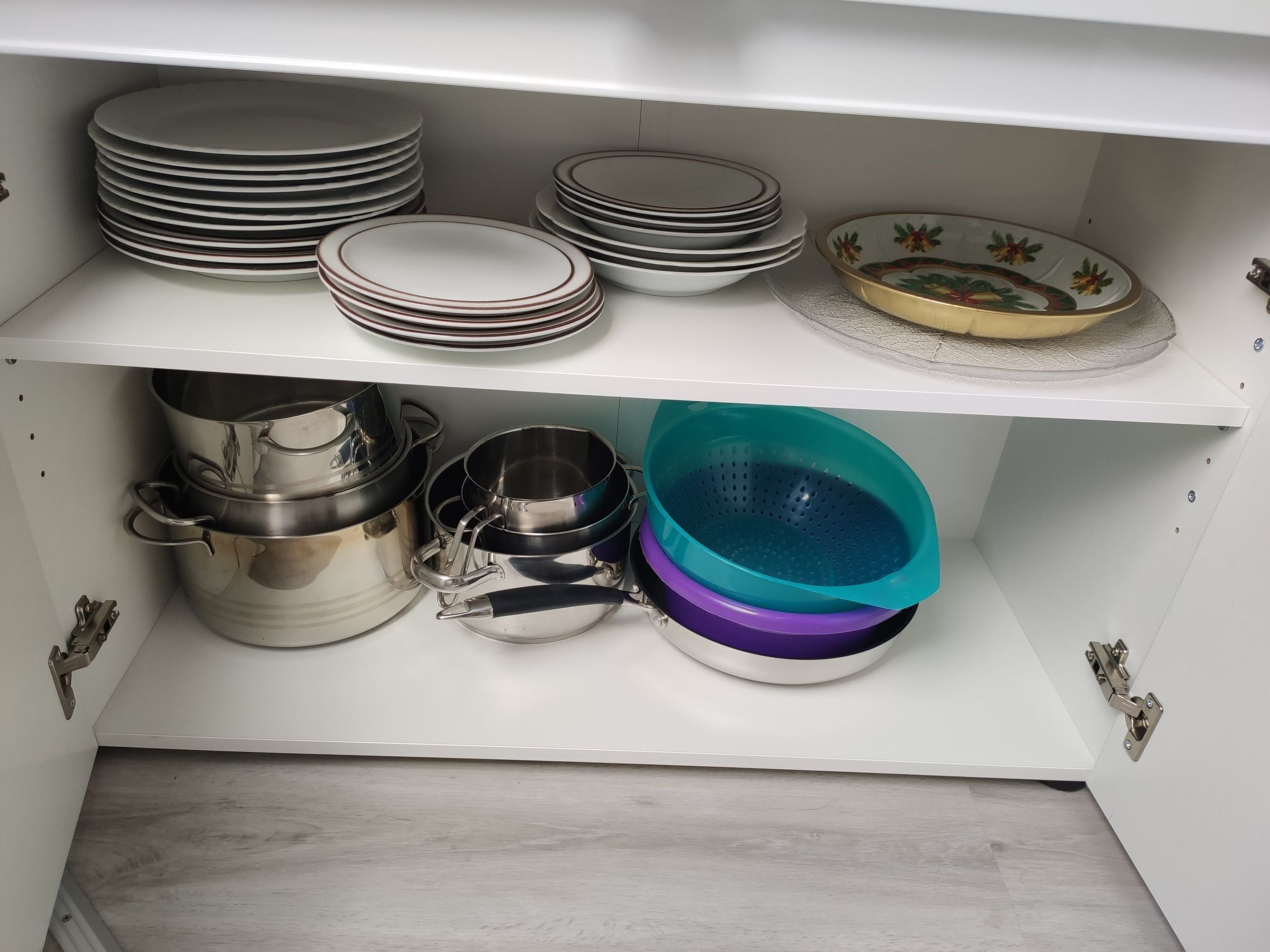 A kitchen cabinet with stacked plates, a decorative plate, and stainless steel cookware.