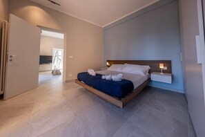 Habitación de hotel moderna con una cama grande, mesitas de noche y vistas al pasillo.