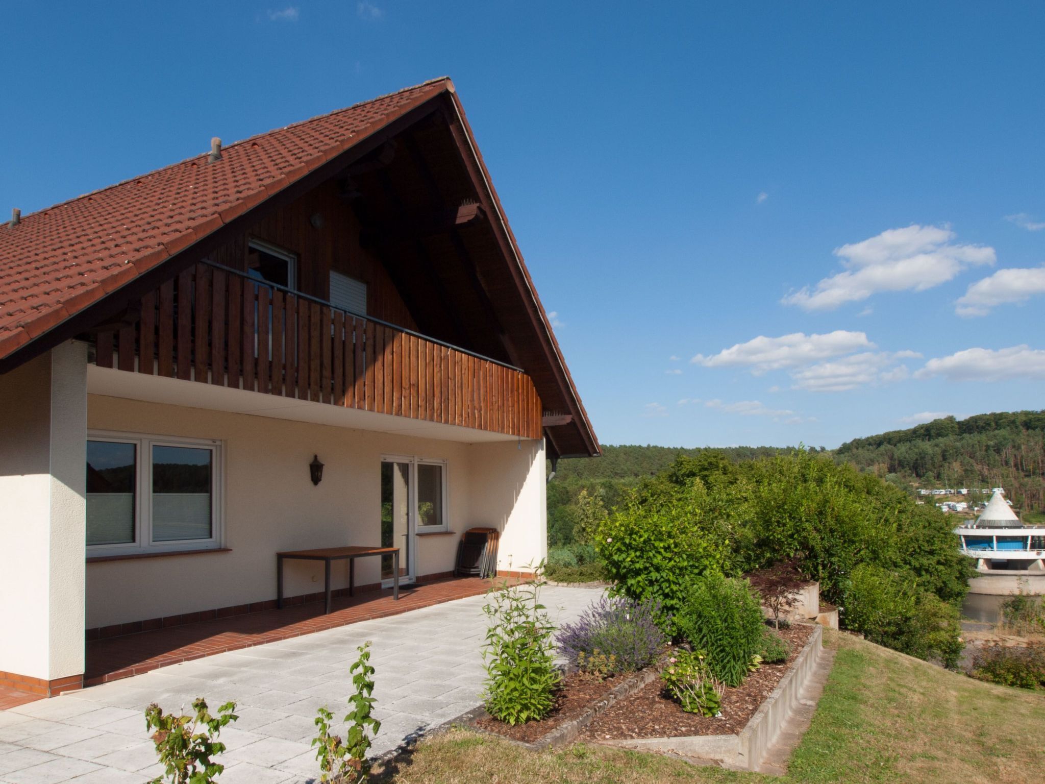 A two-story house with a sloped roof, a balcony, and a view of a lake and hills.