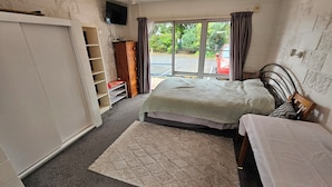 A bedroom with a bed, a wardrobe, a TV, and a view of the outside.