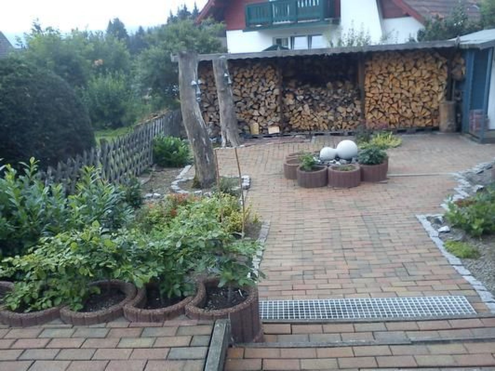 Een betegeld terras met bakstenen vloer, omringd door potplanten en een houten hek.