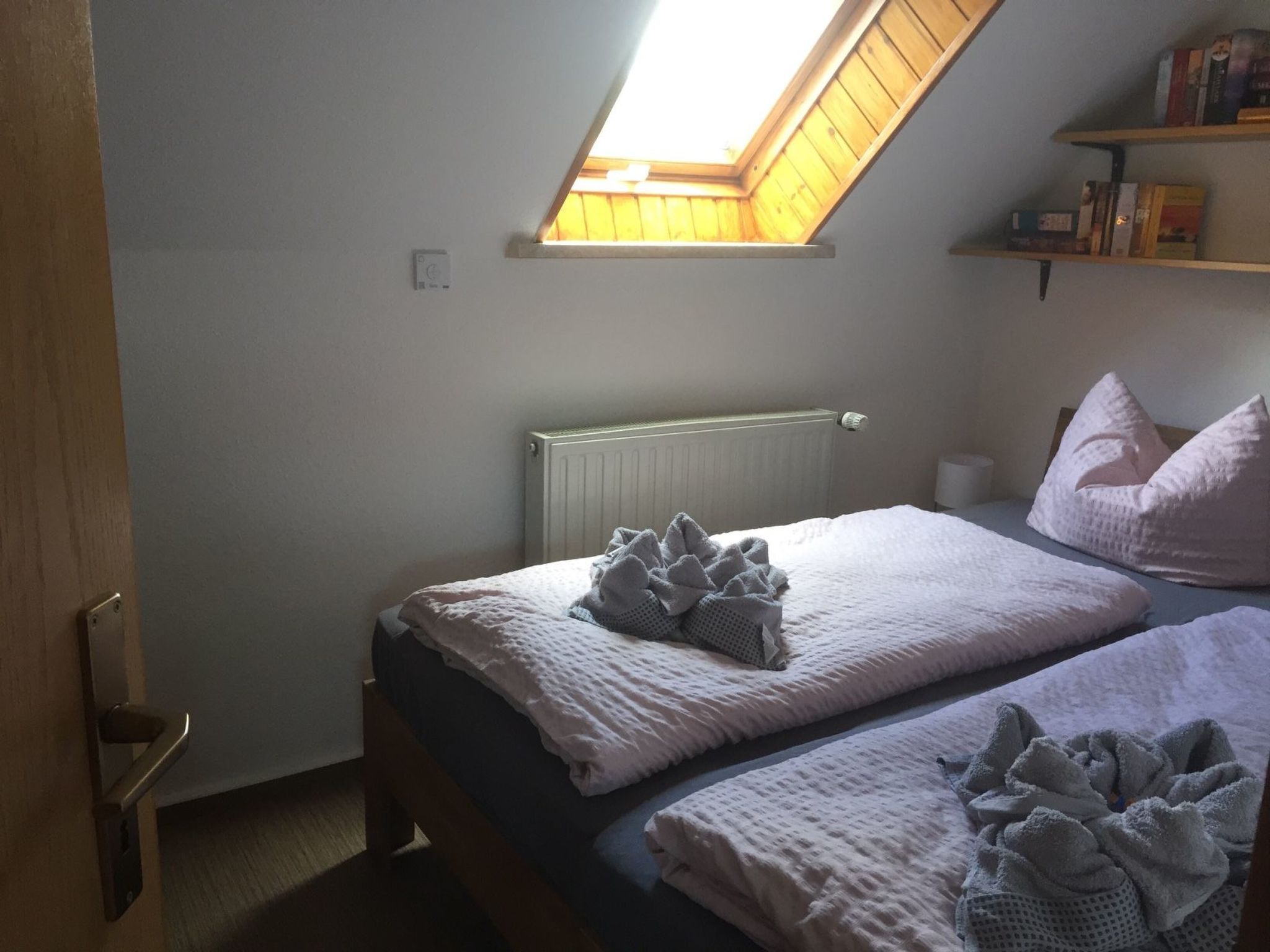 A bedroom with a sloped ceiling, a radiator, a wooden door, and a bookshelf with books.