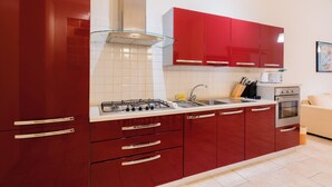 A modern kitchen with red cabinets, a stainless steel range hood, a gas stove, a sink, and a built-in oven. - Suite del Borgo in the heart of the historic center of Tricase (Tricase)