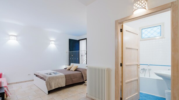 A bedroom with a bed, a radiator, and a bathroom with a bathtub and sink. - Suite del Borgo in the heart of the historic center of Tricase (Tricase)