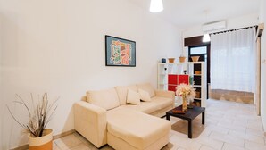 A living room with a beige sofa, a coffee table, a potted plant, a bookshelf, and a framed artwork on the wall. - Suite del Borgo in the heart of the historic center of Tricase (Tricase)