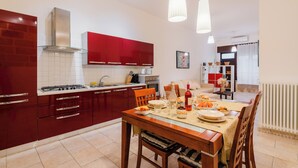 A modern kitchen with red cabinets, a gas stove, and a dining area with a table set for four. - Suite del Borgo in the heart of the historic center of Tricase (Tricase)