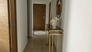 A hallway with a wooden door, a white vase with flowers, and a gold-framed mirror on the wall. - Luxury apartment 170 m² La Marsa - 3 bedrooms, terrace & private parking (La Marsa)