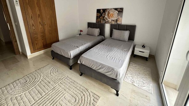 A bedroom with two beds, a wooden wardrobe, a nightstand, a painting, and a rug. - Luxury apartment 170 m² La Marsa - 3 bedrooms, terrace & private parking (La Marsa)