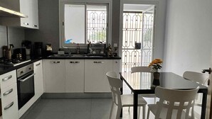 A compact kitchen with white cabinets, a stove, and a sink. There is a window with a view of a metal gate outside. - Luxury apartment 170 m² La Marsa - 3 bedrooms, terrace & private parking (La Marsa)