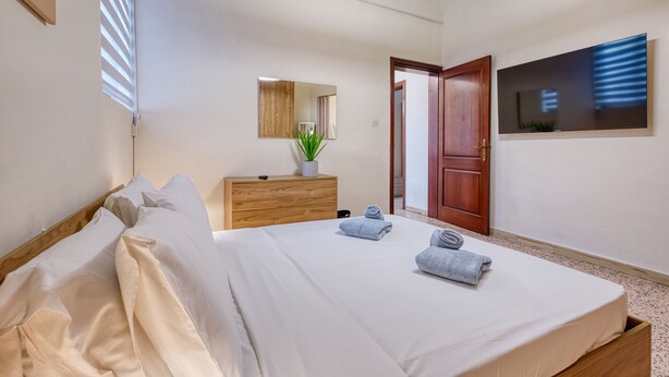 A hotel room with a bed, a wooden dresser, a mirror, a TV, and a door. - Traditional, large 3 bedroom house with Yard JBAR1-1 (St Julian's)