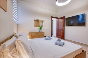 A hotel room with a bed, a wooden dresser, a mirror, a TV, and a door. - Traditional, large 3 bedroom house with Yard JBAR1-1 (St Julian's)