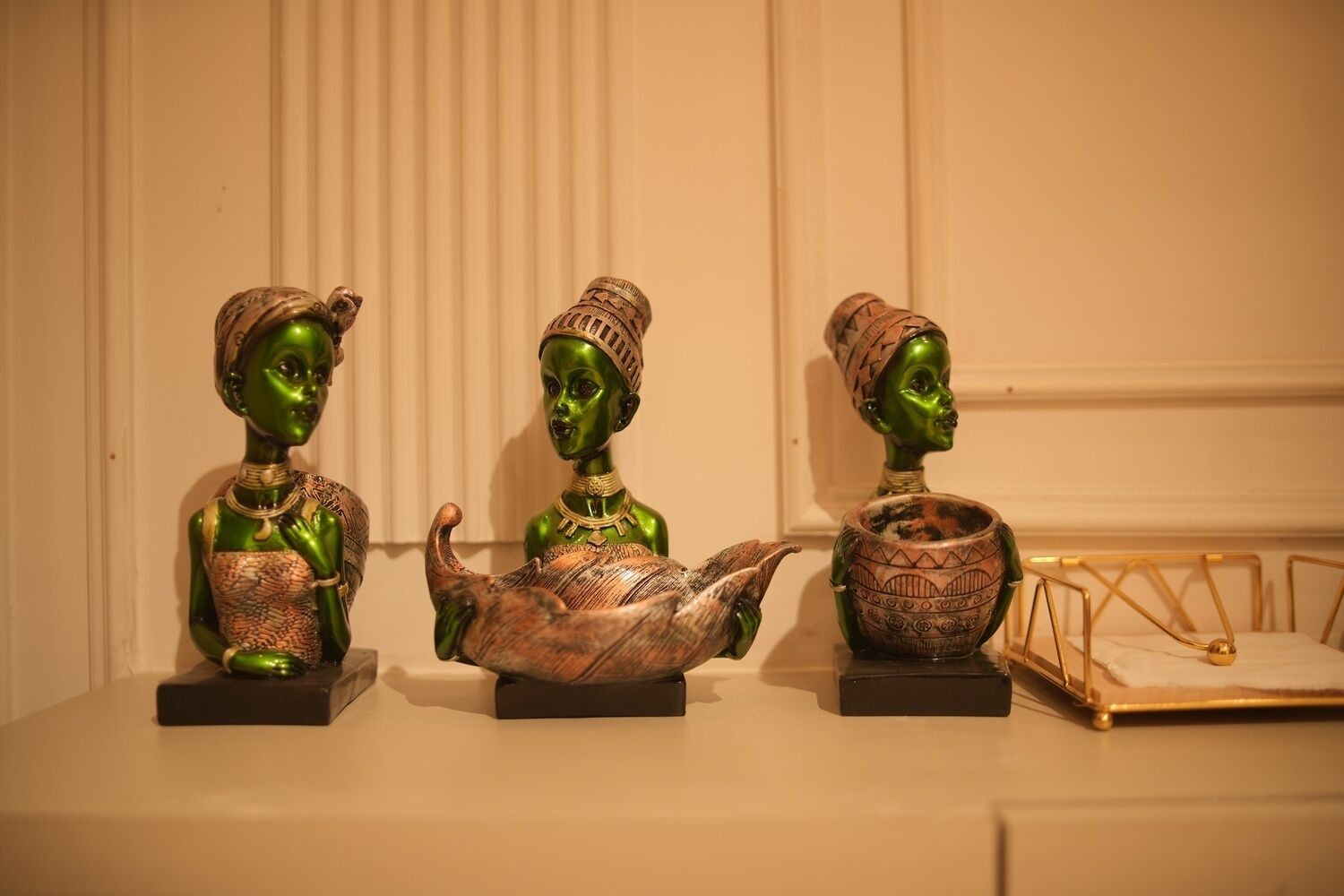 Three green figurines on a table with a decorative bowl and a metal frame.