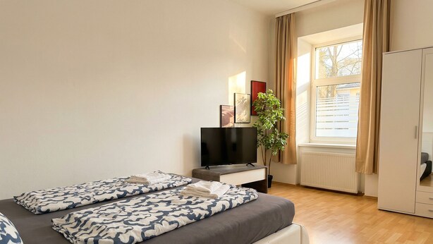 Habitación de hotel con cama, televisión, planta y ventana con cortinas.