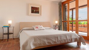 Ein Schlafzimmer mit einem Bett, zwei Nachttischen, einem Wandbild in einem Rahmen und Blick durch ein großes Fenster.