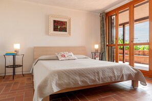 A bedroom with a bed, two bedside tables, a nightstand, a framed picture on the wall, and a view through a large window. - Villa with Private Pool, Wi-Fi, and Air Conditioning in Treggiaia (Treggiaia)