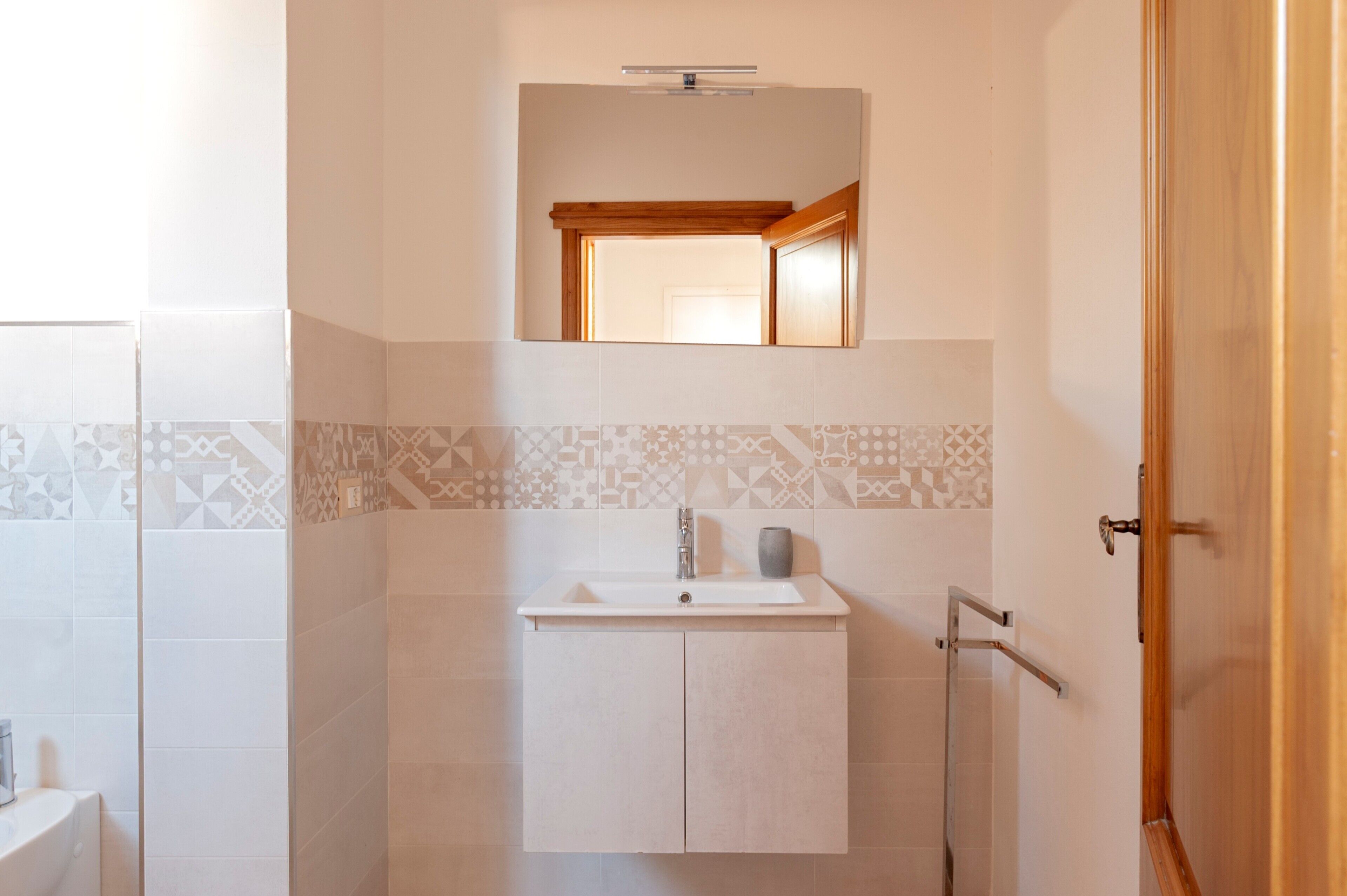 A bathroom with a sink, mirror, and patterned tiles.