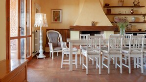 Ein Essbereich mit Tisch, Stühlen, einer Lampe, einem Kamin und Regalen mit Dekoration.