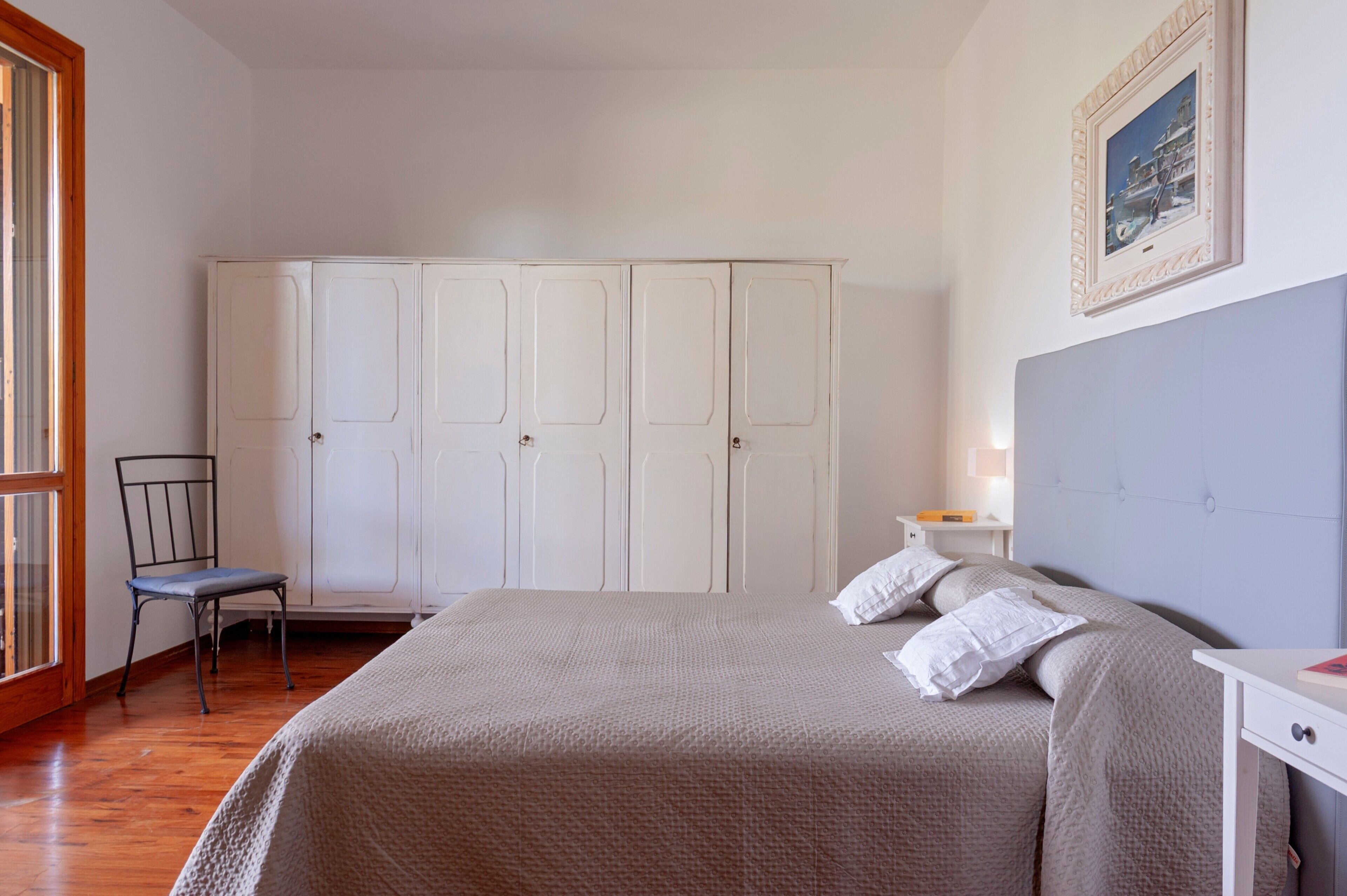 A bedroom with a bed, a chair, a wardrobe, and a nightstand.