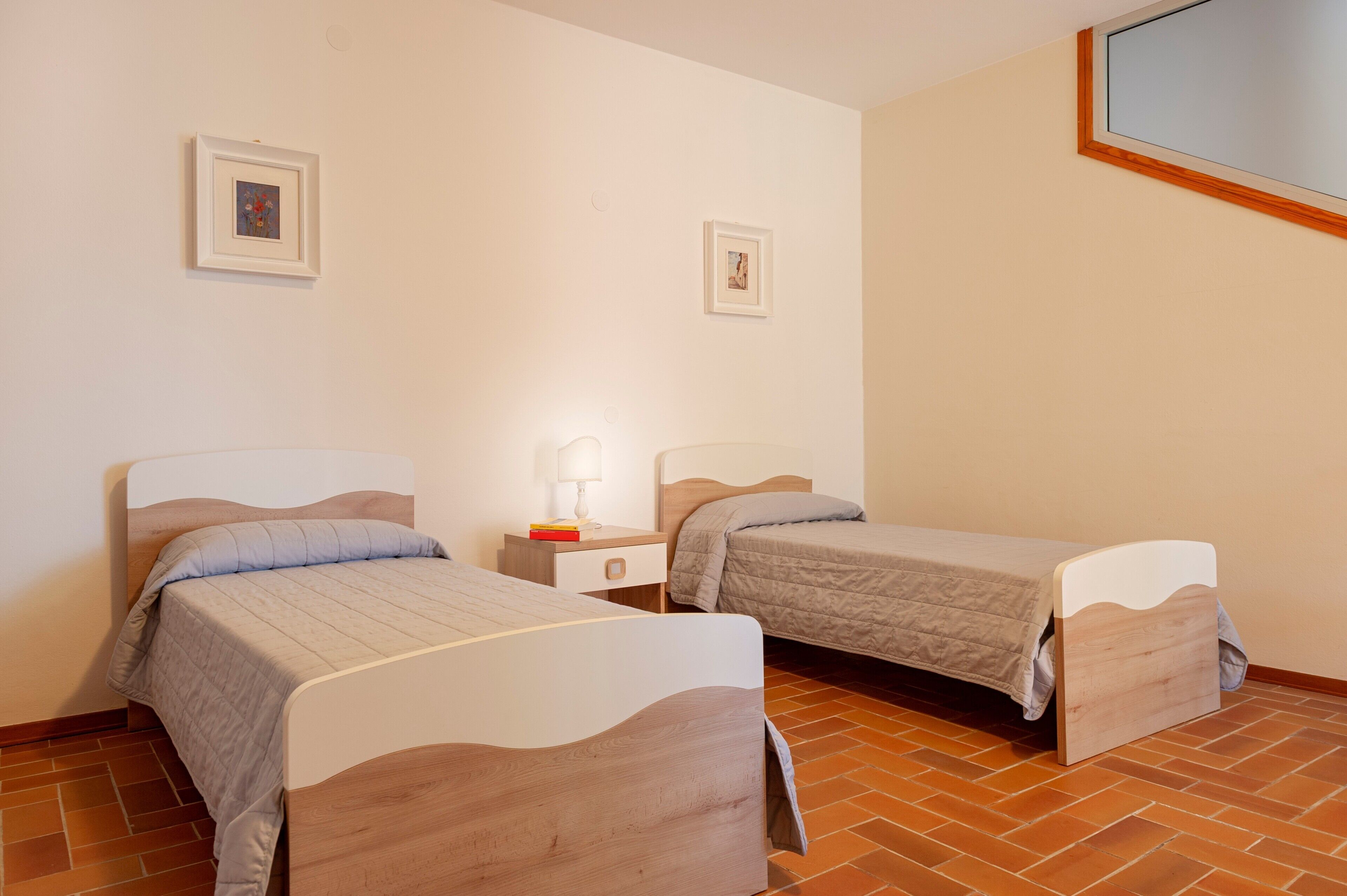 Una habitación con dos camas, una mesita de noche con lámpara y dos cuadros en la pared.