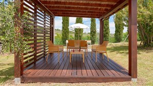 Eine Holzterrasse mit einer Pergola, einem Tisch mit Stühlen und einem weißen Sonnenschirm.