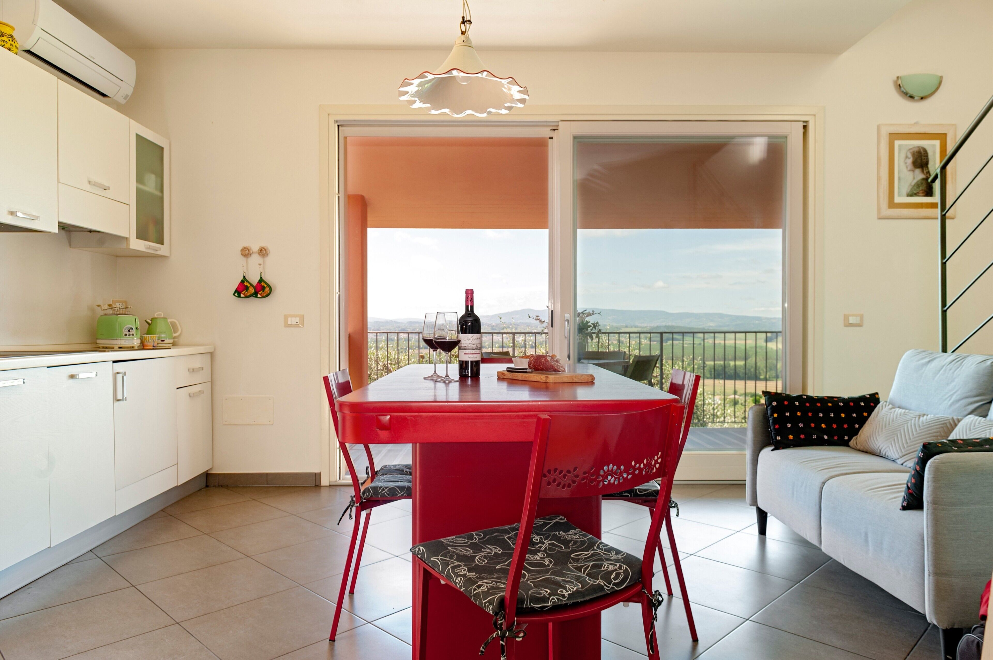 A dining area with a red table and chairs, a wine bottle, and a view through a glass door.