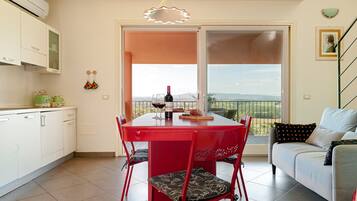 A dining area with a red table and chairs, a wine bottle, and a view through a glass door.