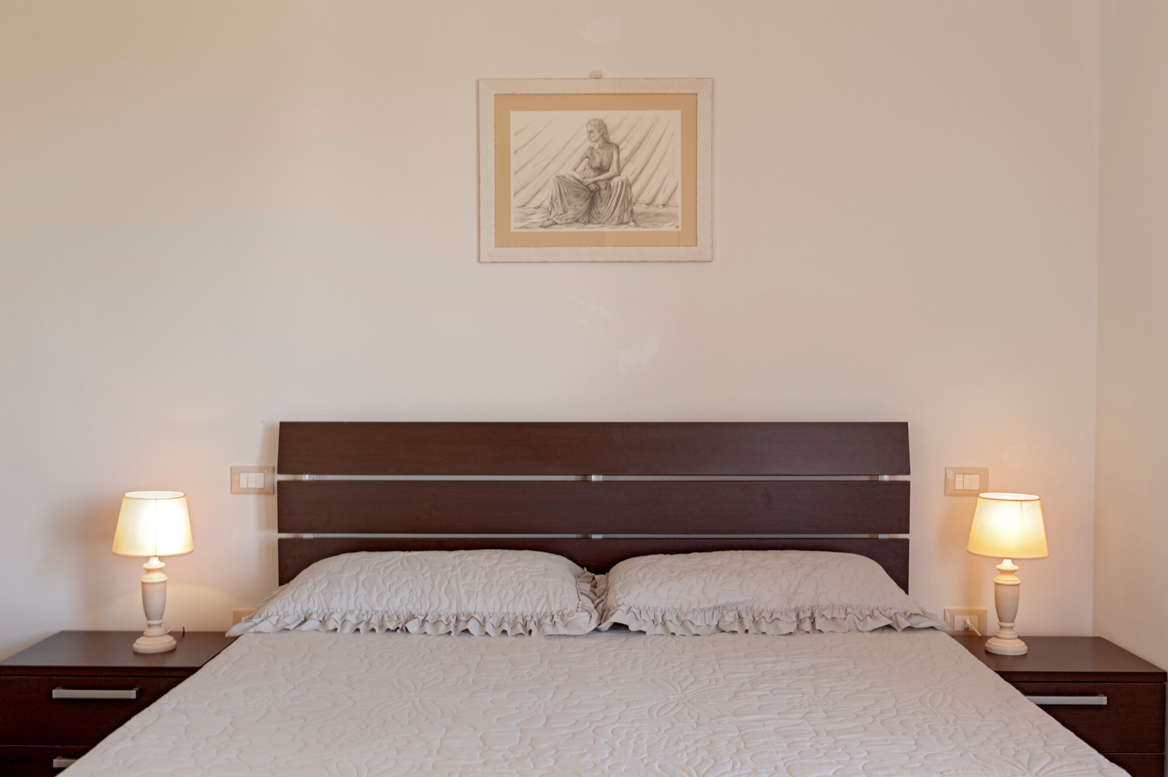 Ein ordentlich bezogenes Bett mit Kopfteil, zwei Nachttische mit Lampen und ein gerahmtes Kunstwerk an der Wand.
