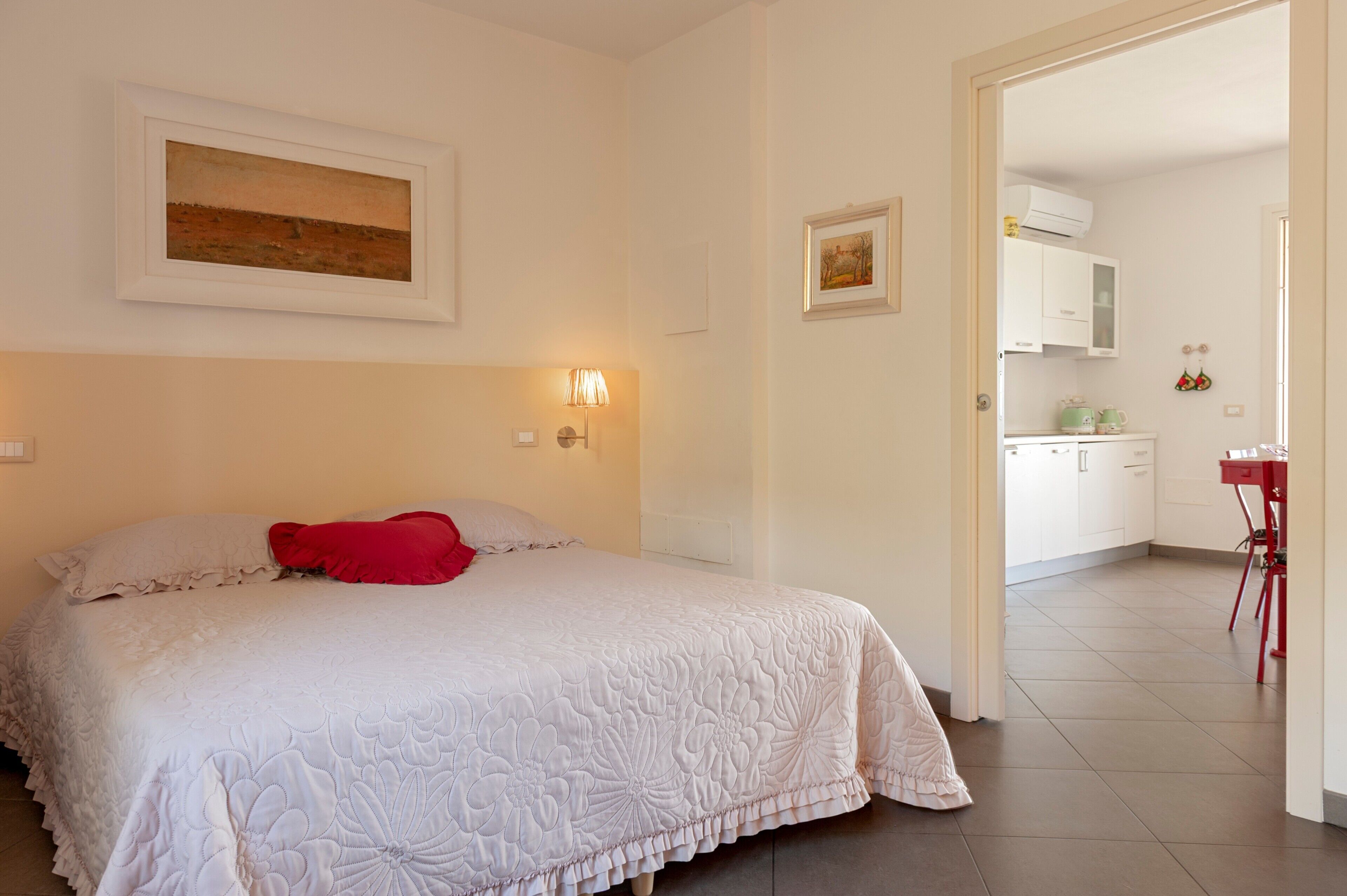 Une chambre à coucher avec un lit, un oreiller rouge, des lampes fixées au mur et un tableau.
