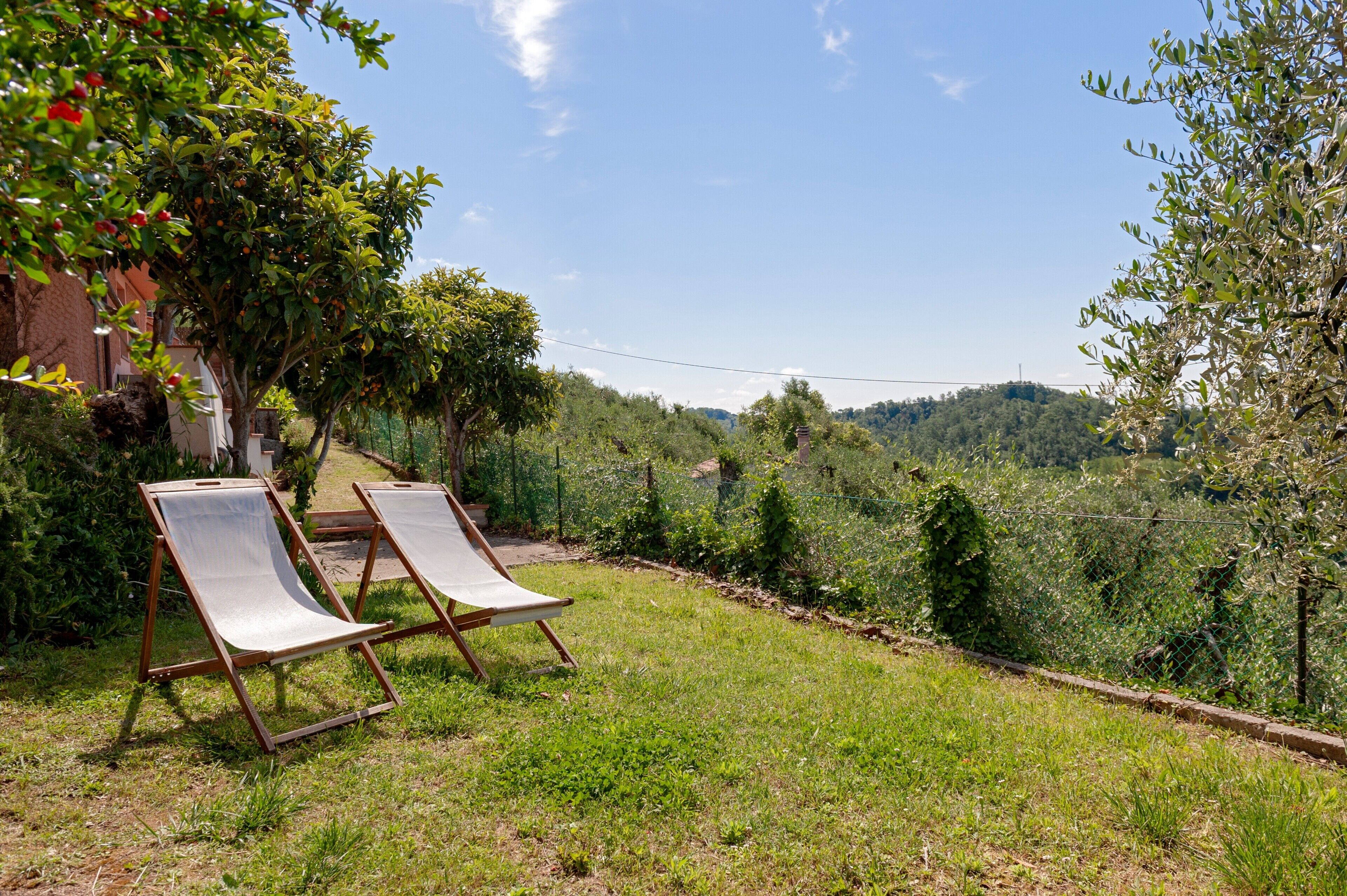 Un jardin avec deux chaises longues en bois, un bâtiment en briques et, au loin, un paysage vallonné.