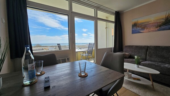 Un salón moderno con una mesa de comedor, sillas, sofá y vistas a la playa a través de grandes ventanales.
