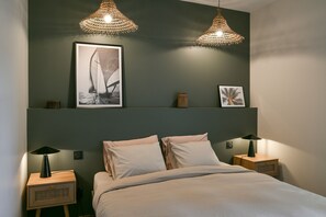 Een slaapkamer met een bed, twee nachtkastjes, een wandplank met ingekaderde foto’s en twee hanglampen.