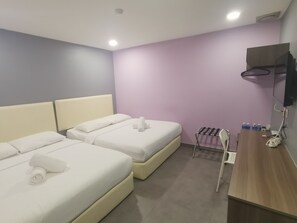A hotel room with two beds, a wooden desk, a TV mounted on the wall, and a small seating area with a chair and a rack holding bottles. - Grand Village Hotel  (Ampang)