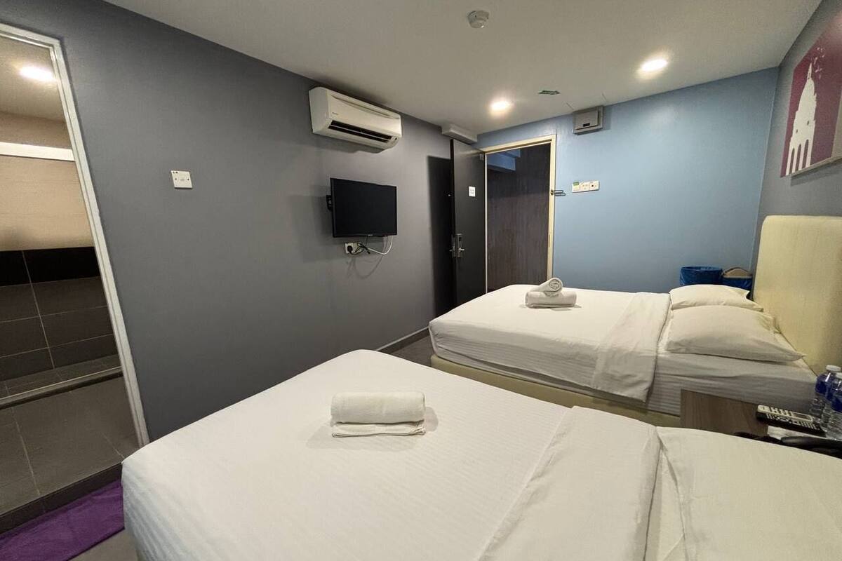 Ein Hotelzimmer mit zwei Betten, einem Flachbildfernseher, einer Klimaanlage und einem Badezimmer mit Dusche.